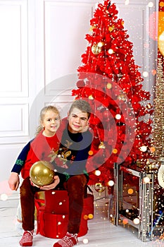 Happy kids girl and teenager, brother and sister smiling in Christmas sweaters playing with a golden ball sitting by the Christmas