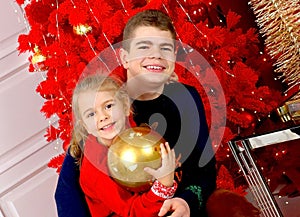 Happy kids girl and teenager, brother and sister smiling in Christmas sweaters playing with a golden ball sitting by the Christmas