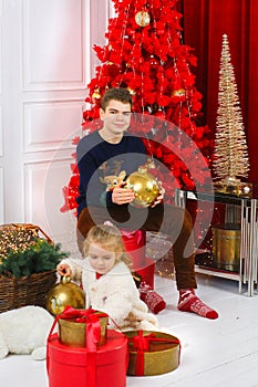 Happy kids girl and teenager, brother and sister smiling in Christmas sweaters playing with a golden ball sitting by the Christmas