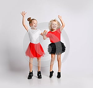 Happy kids girls in fatin skirts and t-shirts are jumping with her hands up playing laughing screaming