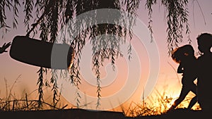 Happy kids having fun outdoor. Little boy and girl playing with swing near the lake during beautiful sunset.