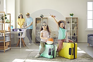 Happy kids having fun with suitcases while parents are getting ready for family holiday trip