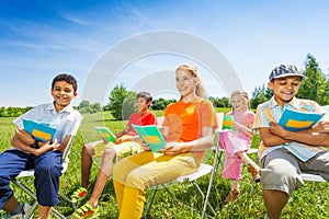 Happy kids hold exercise books and sit on chairs