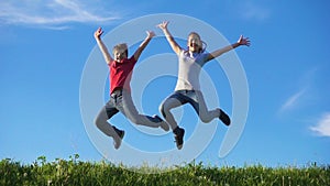 Happy kids jumping on green grass hill against blue sky