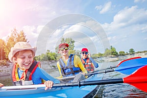 Happy kids kayaking on the river on a sunny day during summer vacation