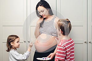 Happy kids painting pregnant belly their mother. Baby birth expecting time and belly painting