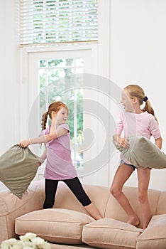 Happy kids, pillow fight and girls playing on sofa in living room together for fun bonding at home. Couch, siblings or