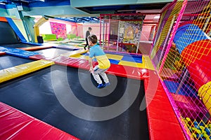 Happy kids playing at indoor play center playground. Boy jumping on trampoline