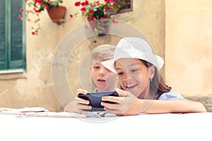 Happy kids playing with momâ€™s smartphone waiting for food at restaurant