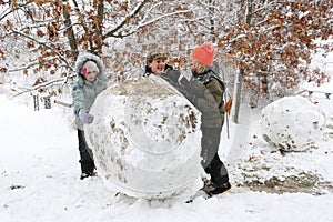 Happy Kids Playing in the Snow Making Huge Snowball