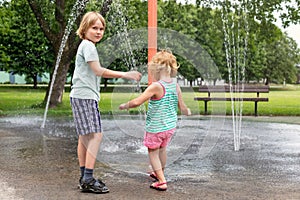 Happy kids playing at water splash pad fountain in park playground on hot summer day