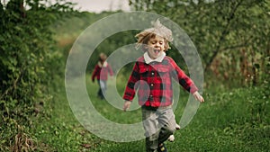 Happy kids running together with beagle puppy in green garden. Smiling brothers, stylish boys having fun with dog