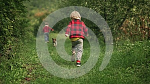 Happy kids running together with beagle puppy in green garden. Smiling brothers, stylish boys having fun with dog