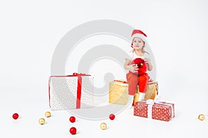 Happy kids in Santas hat sitting on a gift box and holding big red ball. Isolated on white background. Holidays
