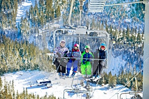Happy kids sit on ski chairlift over winter forest