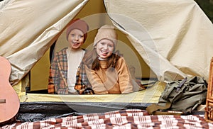 Happy kids sitting in touristic tent and smiling happily at camera during camping trip