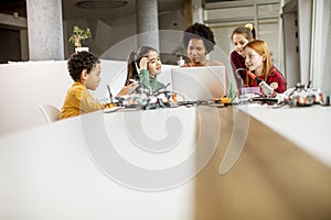 Happy kids with their African American female science teacher with laptop programming electric toys and robots at robotics