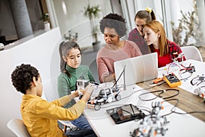 Happy kids with their African American female science teacher with laptop programming electric toys and robots at robotics