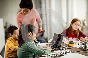 Happy kids with their African American female science teacher with laptop programming electric toys and robots at robotics