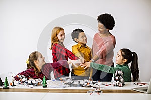 Happy kids with their African American female science teacher  programming electric toys and robots at robotics classroom