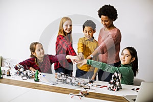 Happy kids with their African American female science teacher  programming electric toys and robots at robotics classroom