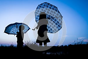 Happy Kids with an umbrella silhouette on nature in the park sunset