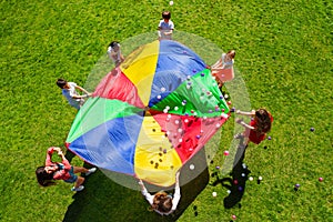 Happy kids waving rainbow parachute full of balls