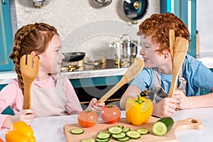 happy kids with wooden utensils smiling each other while cooking together