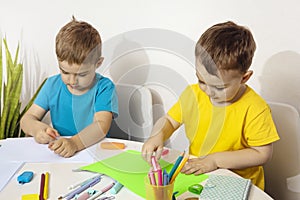 Happy kids with yellow and blue shirts doing arts and crafts together at their desk. Children draw on colored paper