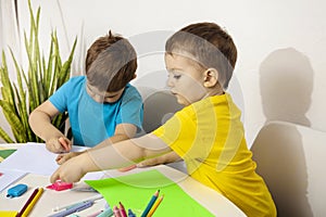 Happy kids with yellow and blue shirts doing arts and crafts together at their desk. Children draw on colored paper