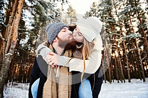 Happy kissing couple. Man giving woman piggyback ride on winter vacation in snowy forest
