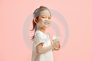 Happy Korean Ethnicity Kid Girl Holding Front of Herself Glass of Milk on Pink  Background photo