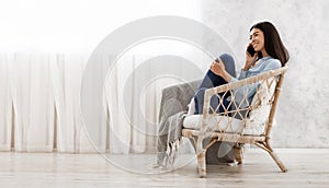 Happy korean girl talking on cellphone at home while relaxing in chair