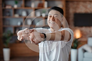 Happy korean mature man stretching arms before domestic training, warming up his hands during home workout