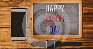 Happy labor day text over wooden slate, smartphone and watch on wooden background