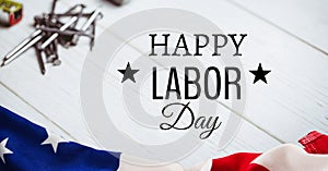 Happy labor day text and tools against american flag on wooden background
