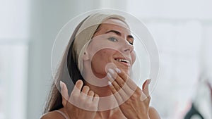 Happy lady applying cream looking mirror at home closeup. Woman touching skin