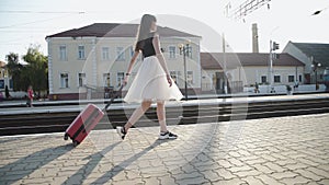 Happy lady in dress goes far with suitcase and whirls on platform