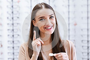 Happy lady holding contact eye lenses in optics shop