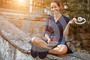 Happy lady resting in park with headset and tablet device. Woman enjoy life on nature. Take break and holiday time idea