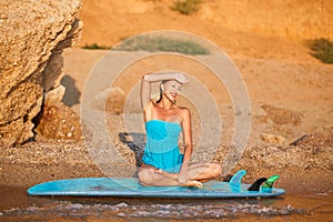 Happy lady sit on beach and enjoying sun. Sandy coastline and board for surf. Adventure time and beach day concept