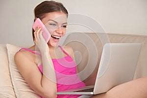 Happy lady talking on cellphone while using laptop