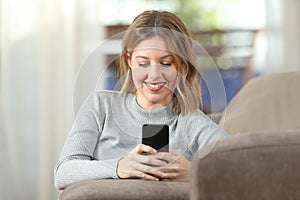 Happy lady texting on phone on a couch at home