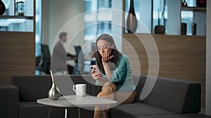 Happy lady watching smartphone at office sofa. Woman rejoicing success alone