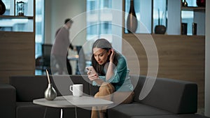 Happy lady watching smartphone at office sofa. Woman rejoicing success alone