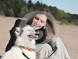 happy laika dog smiling and sitting next to its owner. young beautiful woman stroking her dog sitting on a sandy beach