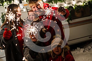 Happy large family celebrates christmas in nature and holds sparklers. Parents with three sons travels in a mobile home.