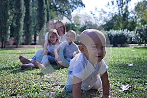 Happy, large family of five sitting on the lawn of a park, laughing as they watch the youngest one crawling away. Concept family,