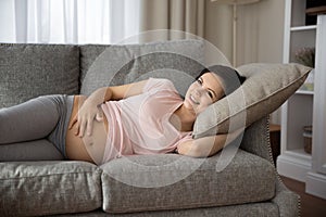 Happy late pregnant woman lying on sofa, relaxing at home