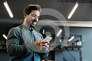 Happy Latin business man executive employee using cell phone standing in office.